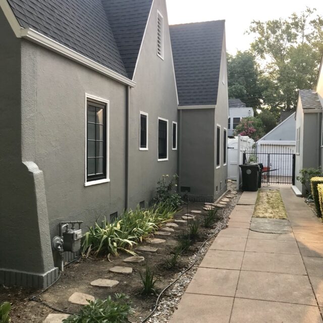 Exterior house painting in Sacramento, CA by Baldwin Custom Painting — close-up of a house corner with dark gray shingles, light gray stucco, and white trim