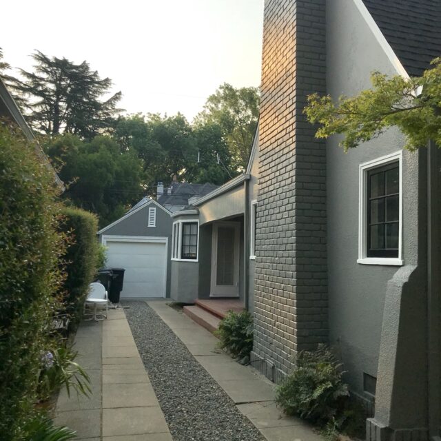 Exterior house painting in Sacramento, CA by Baldwin Custom Painting — tall dark-painted brick chimney beside a gray stucco home with a dark shingle roof