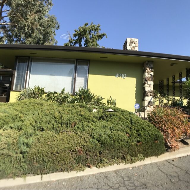 Exterior house painting in Sacramento, CA by Baldwin Custom Painting — mid-century modern home with lime-green stucco siding, dark trim, and a stone chimney