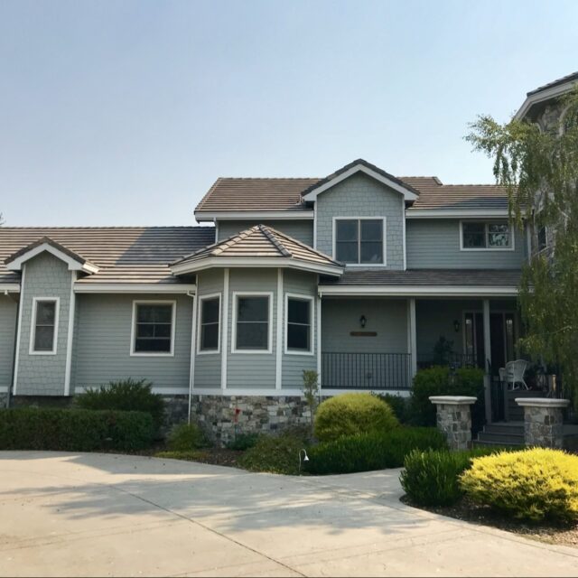 Exterior house painting in Sacramento, CA by Baldwin Custom Painting — two-story craftsman home with sage-green siding, white trim, and a stone base