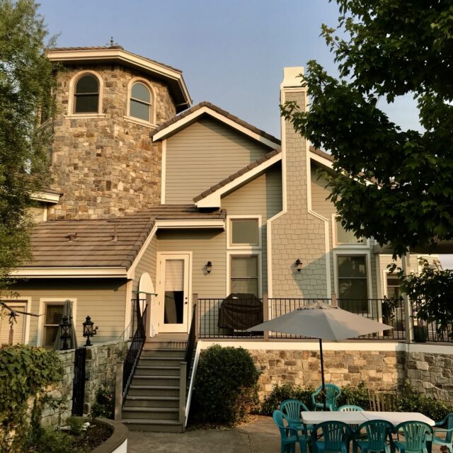 Exterior house painting in Sacramento, CA by Baldwin Custom Painting — two-story home with a stone turret, beige siding, and a light brick chimney