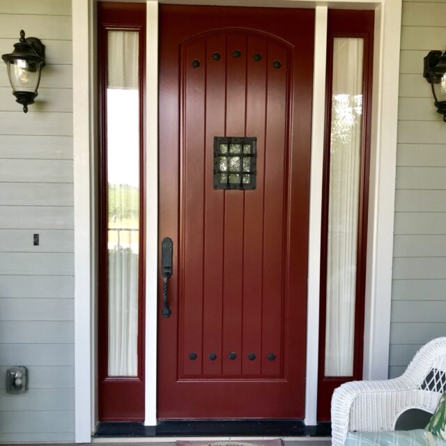 Exterior house painting in Sacramento, CA by Baldwin Custom Painting — close-up of a deep red arched front door with sidelights and lantern sconces, sage-green siding