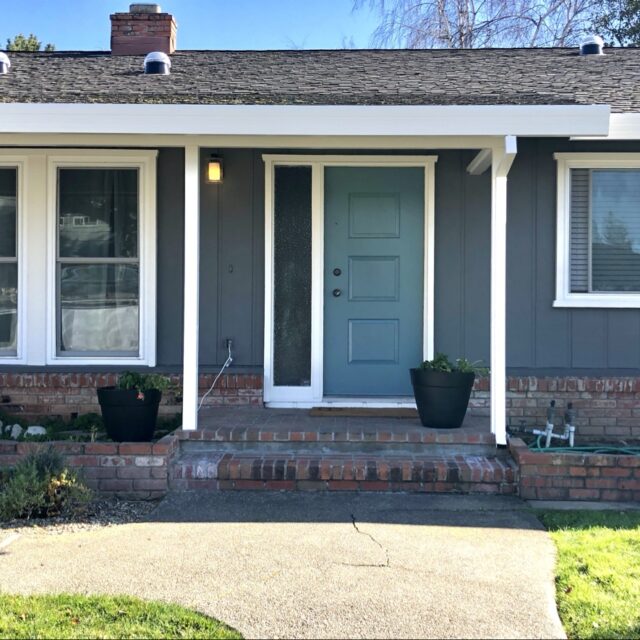 Exterior house painting in Sacramento, CA by Baldwin Custom Painting — ranch-style home with dark gray siding, white trim, and a teal front door
