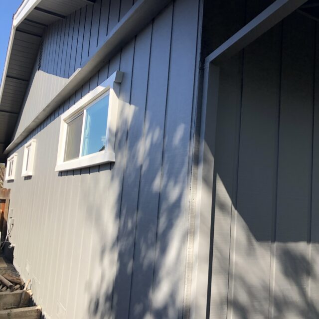 Exterior house painting in Sacramento, CA by Baldwin Custom Painting — close-up of dark gray painted vertical siding under the eave, with soffit and fascia