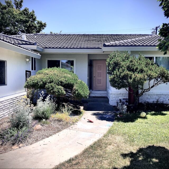 Exterior house painting in Sacramento, CA by Baldwin Custom Painting — single-story ranch home with light gray stucco, a dark tile roof, and a pink front door