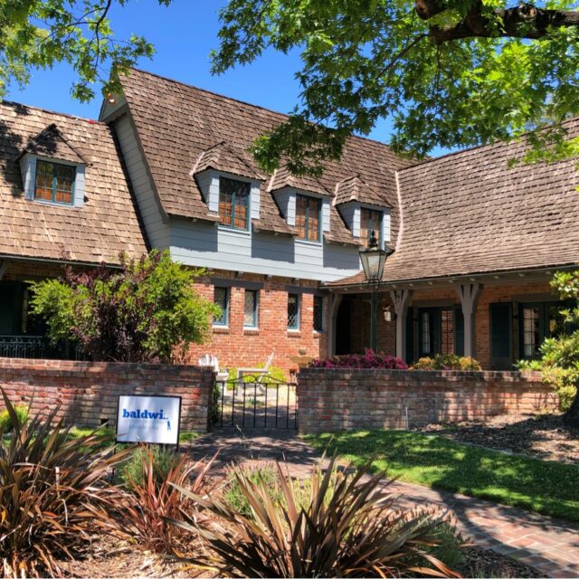 Exterior house painting in Sacramento, CA by Baldwin Custom Painting — brick Tudor-style home with a steep wood-shake roof, dormers, and light blue upper siding