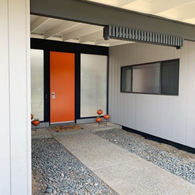 Exterior house painting in Sacramento, CA by Baldwin Custom Painting — mid-century modern entryway with bold orange front door, gray siding, and exposed beam porch ceiling