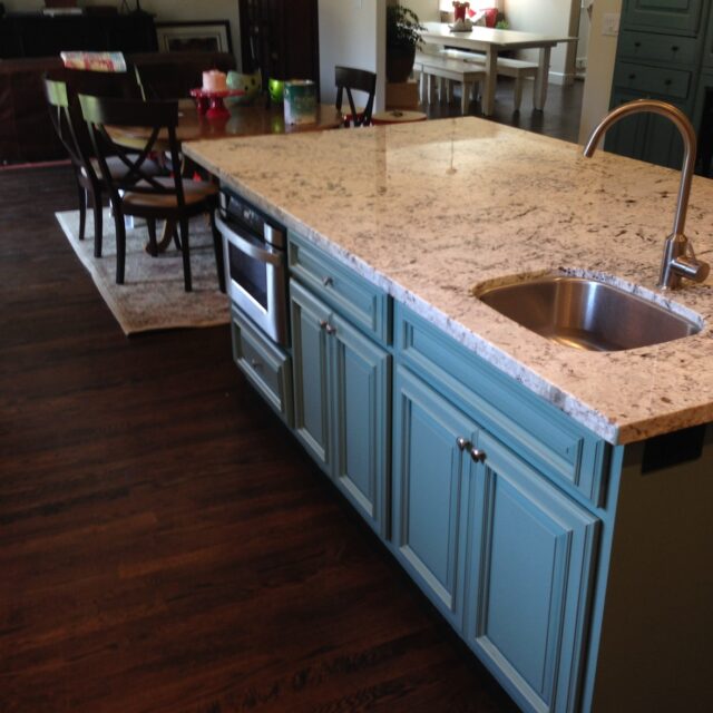 Interior house painting in Sacramento, CA by Baldwin Custom Painting — kitchen with blue-gray painted island cabinets, granite countertops and stainless fixtures, open to a bright dining area