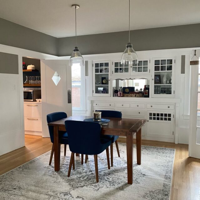 Interior house painting in Sacramento, CA by Baldwin Custom Painting — kitchen with gray-green walls, glass pendant lights and white built-in glass-front cabinets