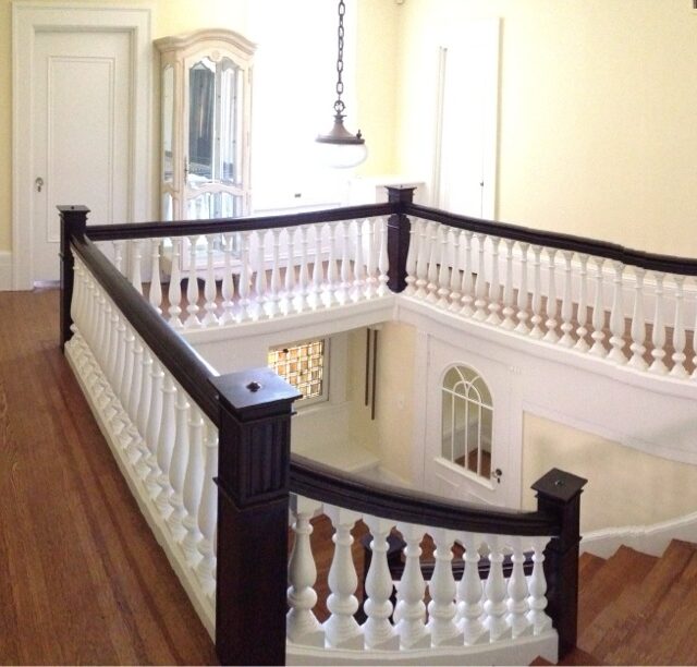 Interior house painting in Sacramento, CA by Baldwin Custom Painting — upstairs landing with white painted balusters, dark wood handrail, cream walls and hardwood floors